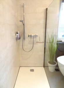 Badezimmer mit Dusche und freistehender Badewanne, Duschwand aus Glas, Duschgestänge, Fliesen in beige (Wand) braun (Boden)